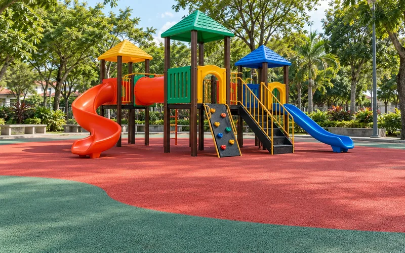 Playground com escorregadores e torres coloridas sobre piso emborrachado contínuo vermelho e verde, em área arborizada