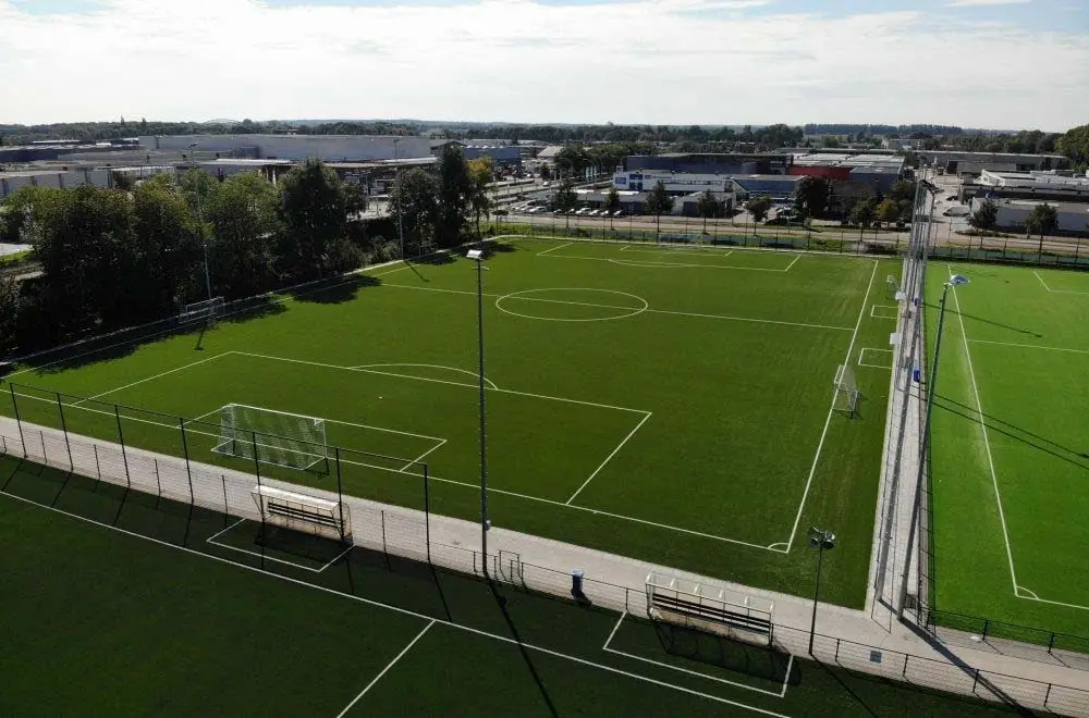 Vista aérea de dois campos de futebol de grama sintética com alambrado, bancos de reserva e torres de iluminação
