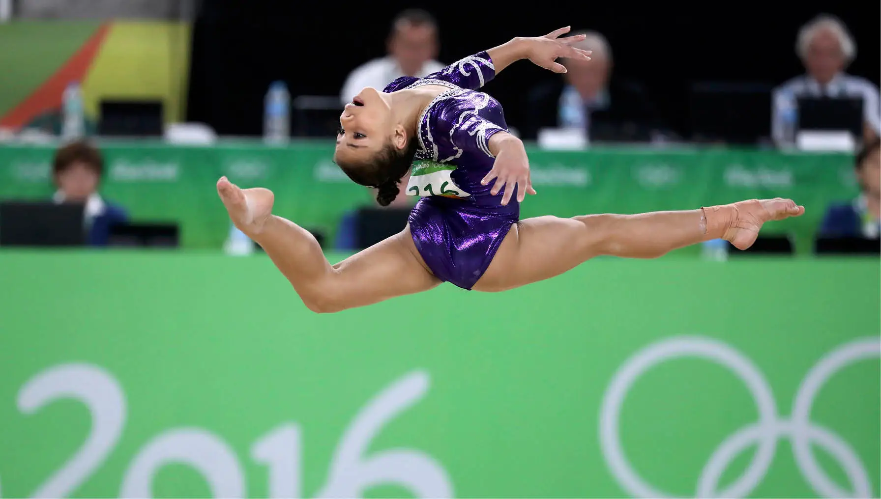Ginasta brasileira em salto com as pernas abertas durante a prova de solo dos Jogos Rio 2016, com a mesa de árbitros ao fundo