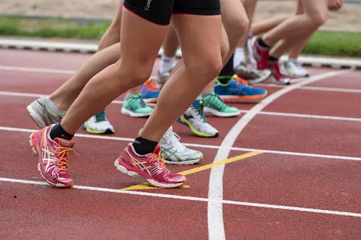Pés de corredores com tênis coloridos na largada de uma pista de atletismo sintética vermelha