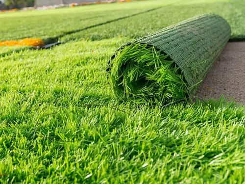 Rolo de grama sintética parcialmente aberto sobre um campo já gramado, com a manta enrolada mostrando a espessura dos fios