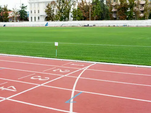 Raias numeradas de uma pista sintética vermelha de atletismo, com gramado e arquibancada ao fundo