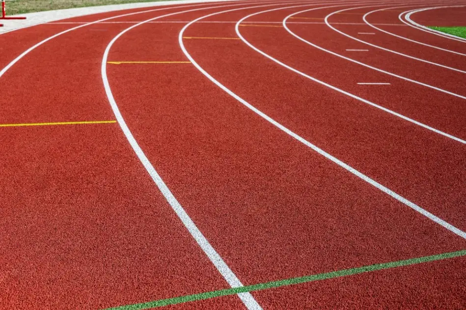 Curva de pista de atletismo vermelha com raias brancas e gramado ao fundo