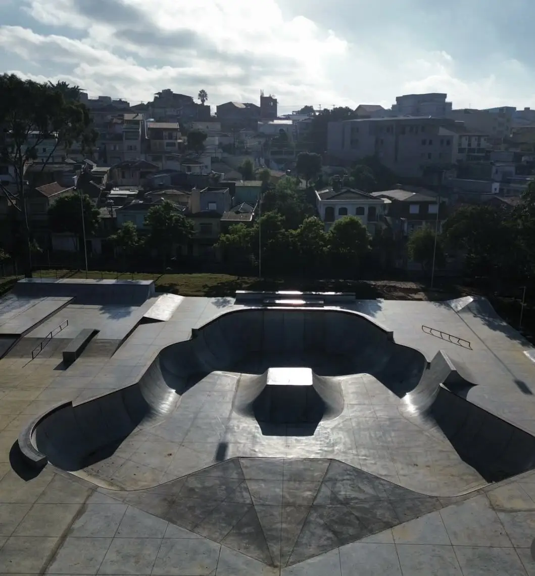 Bowl de concreto liso com borda metálica e ilha central, visto do alto, com casas de bairro ao fundo
